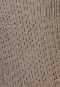 Beige stickad tyg med kabelmönster löpande vertikalt. Texturen är mjuk och något elastisk, vilket ger en ribbad effekt.