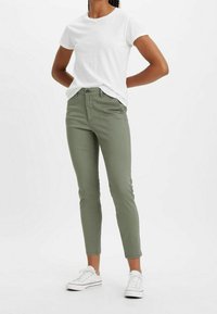 Olivgrön, slim-fit bomullsbyxor med medelhög midja, kompletterade med en vit t-shirt med kort ärm och vita sneakers.