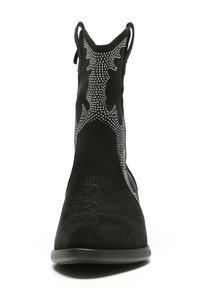 Botín de ante negro con detalles de tachuelas, punta afilada y lengüetas para facilitar el calzado. Presenta una superficie texturizada y costuras decorativas.