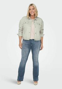 Chaqueta de mezclilla gris clara con botones en el frente, dos bolsillos en el pecho, mangas enrolladas, combinada con una blusa clara y jeans de campana azules. Zapatos de color neutro.