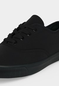 Μαύρο χαμηλό αθλητικό παπούτσι με κορδόνια, λείο ανώτερο υλικό και λαστιχένια σόλα με υφασμένη προστασία μύτης.