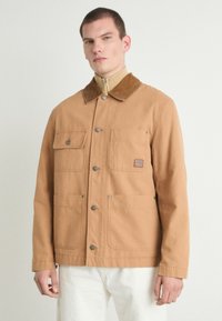 Bruine katoenjack met een corduroy kraag, drukknoopsluiting, twee voorzakken en een gestikt labeldetail. Schoon, recht gesneden ontwerp.