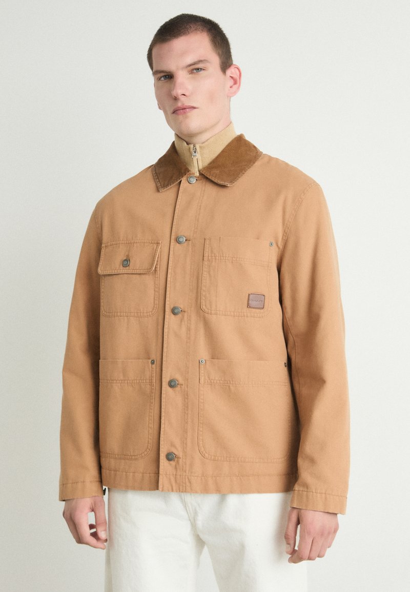 Bruine katoenjack met een corduroy kraag, drukknoopsluiting, twee voorzakken en een gestikt labeldetail. Schoon, recht gesneden ontwerp.