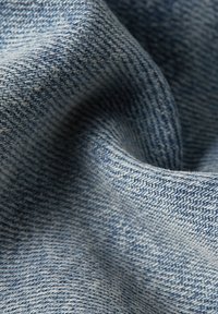Tissu en denim dans des nuances de bleu avec un tissage texturé, mettant en évidence un gros plan de la surface du matériau et des fibres fines entrelacées.