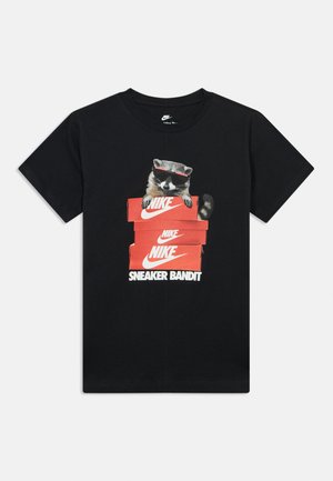 Μαύρη μπλούζα Nike με γραφικό ενός ρακούν που φοράει γυαλιά ηλίου και κρυφοκοιτάζει από στοιβαγμένα κόκκινα κουτιά παπουτσιών Nike με κείμενο "SNEAKER BANDIT."