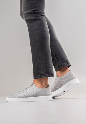 Grijze mesh sneakers met vetersluiting, witte rubberen zool en gestructureerde afwerking. Gecombineerd met slim-fit donkergrijze jeans.