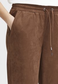 Brown sweatpants made of soft, suede-like material. Features an elastic waistband, drawstring, and side pockets.