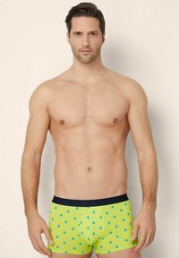 Grüne Boxershorts mit einem blauen Fruchtmuster und einem dunkelblauen Bund. Der Stoff ist glatt und hat ein enganliegendes Design.