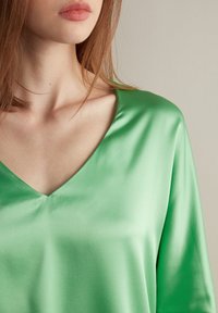 Chemisier en satin vert avec un décolleté en V profond et une texture douce et lisse. Le tissu a une finition brillante, améliorant l'apparence générale.