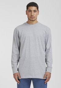 Camiseta de manga larga gris hecha de algod�ón, con un escote redondo y un corte relajado, combinada con jeans de mezclilla azules.