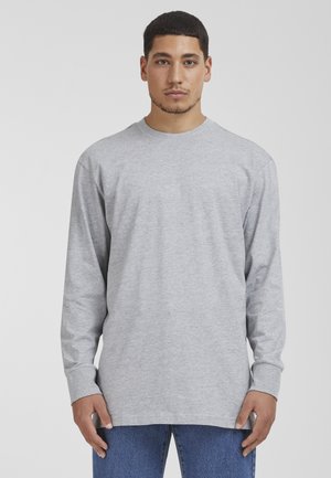 Camiseta de manga larga gris hecha de algodón, con un escote redondo y un corte relajado, combinada con jeans de mezclilla azules.