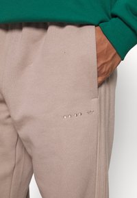 Pantalones jogger beige con una textura suave, que presentan tres puntos en relieve y un pequeño logo en el muslo. Acabados con tejido verde oscuro en la parte superior.