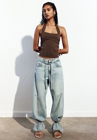 Barna pánt nélküli crop top, világoskék, bőszárú farmernadrág húzózsinórral a deréknál, és bézs magas sarkú szandál ráncolt részletekkel.