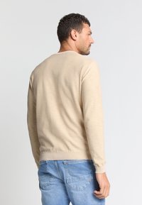Beige lange mouwen sweater met een geribbelde halslijn en manchetten, gemaakt van textiel stof, gedragen met lichtblauwe spijkerbroek.