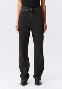 Calças de ganga pretas de cintura alta com corte de perna direita, tecido resistente, costuras subtis e cinco bolsos; fecho de botão e fecho éclair.