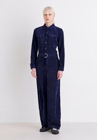 Marineblauw corduroy jumpsuit met een getailleerde taille, lange mouwen, knoopsluiting aan de voorkant, twee borstzakken en een wijde pijp.