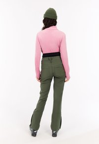 Roze geribbelde top met lange mouwen, zwarte tailleband, gecombineerd met olijfgroene broeken met achterzakken en splissen bij de enkels. Groene gebreide muts.
