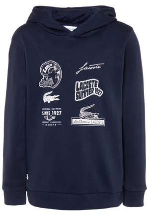 Námořnická modrá mikina s kapucí vyrobená z měkké tkaniny, s bílými grafickými potisky a textem, včetně loga krokodýla a různých designů.