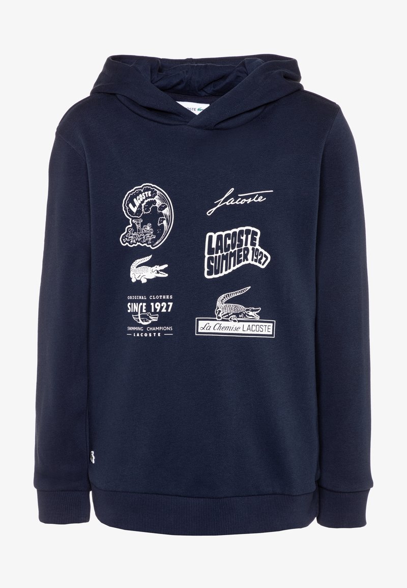 Námořnická modrá mikina s kapucí vyrobená z měkké tkaniny, s bílými grafickými potisky a textem, včetně loga krokodýla a různých designů.