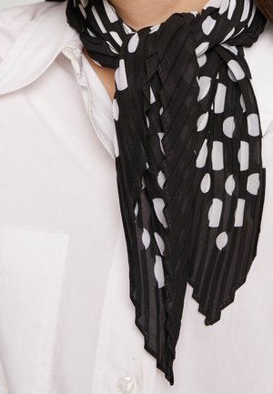 Écharpe noire à pois blancs nouée autour du cou sur une chemise blanche à col.