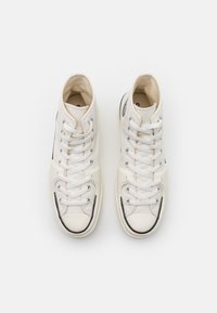 High-top sneakers in off-white canvas with grey accents, metal eyelets, flat laces, and textured rubber toe cap. Black rubber outsole.