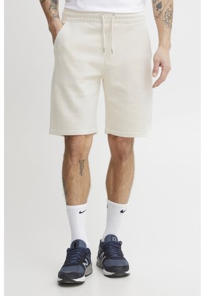 Pantaloni corti in tessuto morbido color crema, con vita elastica e cordoncino, e tasche laterali. Texture liscia, taglio alla lunghezza del ginocchio.