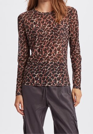 Femme portant un haut à manches longues imprimé léopard marron et noir associé à un pantalon ample gris foncé avec des poches latérales.