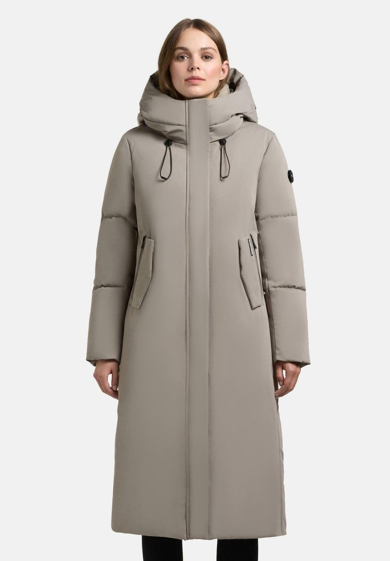 Lang beige pufferjakke med hætte, der har lynlås foran, sidelommer og justerbare snore. Glat tekstur, minimalistisk design.