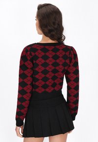 Sarkans un melns argyle raksts džemperis ar pūkainām piedurknēm, ribotām apkaklēm un apakšmalu. Kombinēts ar noberztu melnu svārku.