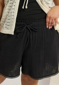 Svarta, texturerade shorts med dragsko i midjan och scallop-lace kant. Tillverkade av ett lättviktigt material, med vertikala ränder.