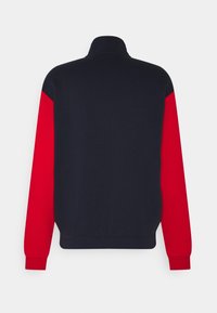 Chaqueta de pullover en azul marino y rojo con cuello alto. Presenta una textura suave y mangas largas con bloques de color en contraste en cada brazo.