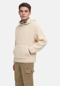 Haut en polaire crème avec une poche kangourou, un logo en relief et une capuche avec cordon de serrage, associé à un pantalon cargo beige avec une poche à rabat.