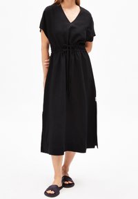 Czarna bawełniana sukienka midi z dekoltem w serek, krótkimi rękawami, regulowanym paskiem w talii oraz bocznymi rozcięciami, w połączeniu z ciemnymi klapkami.
