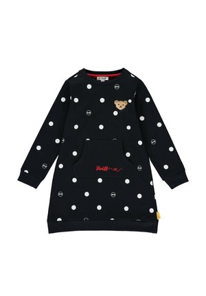 Robe noire à manches longues avec des pois blancs, poche avant avec broderie rouge "Steiff" et petit écusson ourson sur la poitrine.