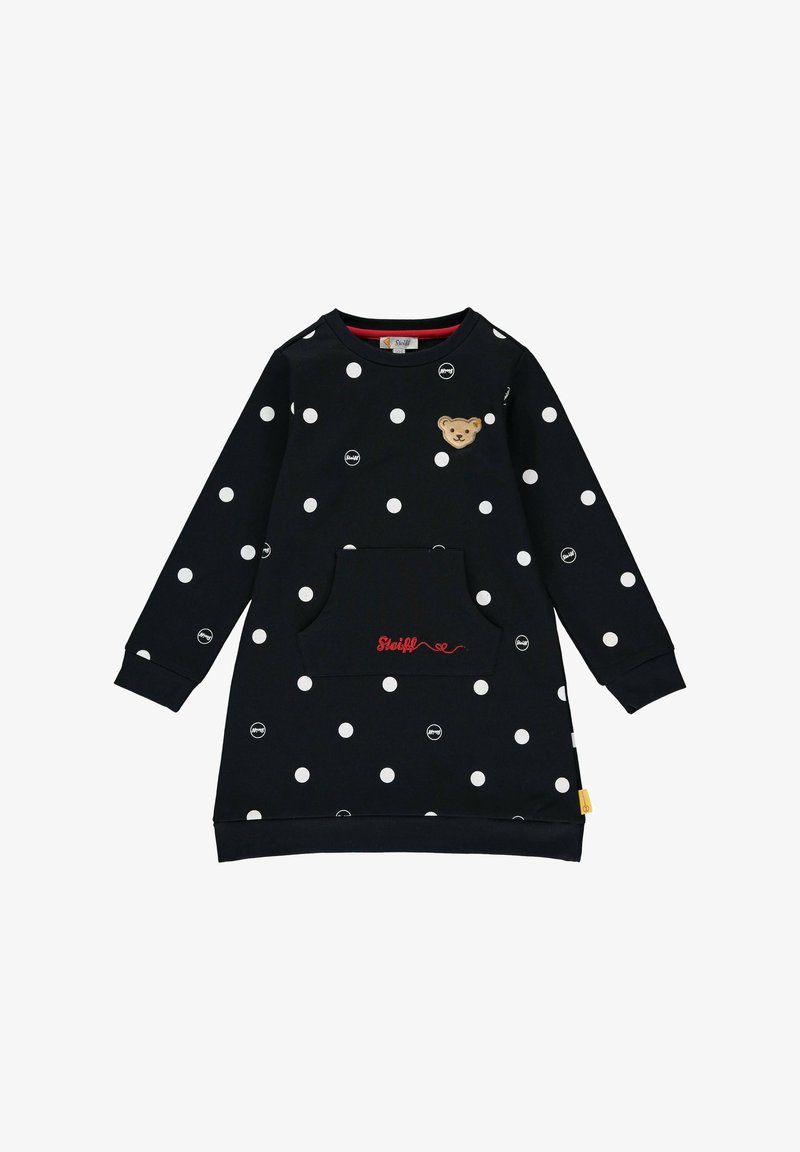 Robe noire à manches longues avec des pois blancs, poche avant avec broderie rouge "Steiff" et petit écusson ourson sur la poitrine.