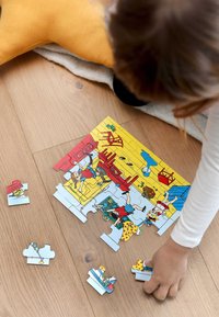 Farverige puslespilsbrikker på lys trægulv, der viser legende scener med tegneseriefigurer. Nærliggende brikker er spredt omkring.