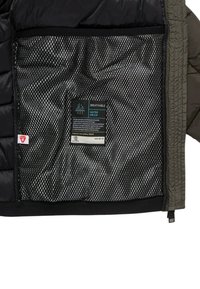 Interno di giacca nero e verde oliva che mostra una tasca in rete traspirante. Presenta un'etichetta impermeabile con istruzioni per la cura e informazioni sul tessuto.