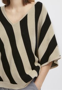 Beżowy i czarny sweter w paski w oversize'owym rozmiarze z dekoltem w kształcie litery V i krótkimi rękawami, cechujący się miękką fakturą i luźnym krojem.