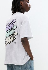 Gray cotton t-shirt with short sleeves, featuring colorful graffiti-style text on the back; relaxed fit and smooth texture.
