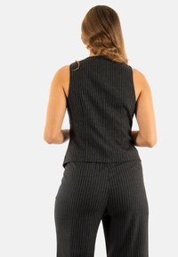 Blusa sin mangas de rayas negras combinada con pantalones a juego, con un corte entallado y una textura suave, mostrada desde atrás.