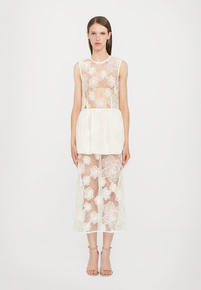 Abito in pizzo floreale trasparente con vita solida, design senza maniche e dettagli a volants a più livelli. I colori sono prevalentemente bianchi con motivi floreali.