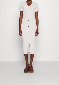 Rippiertes, kurzärmliges, weißes Kleid mit V-Ausschnitt, Knöpfen vorn und einem Schlitz. Kombiniert mit braunen Plateausandalen.