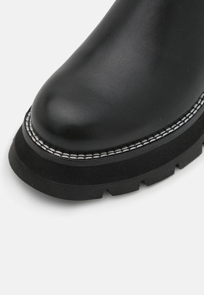 Μαύρο δερμάτινο μποτάκι μέχρι τον αστράγαλο με στρογγυλή μύτη, υφή στην επάνω πλευρά και χοντρή μαύρη καουτσούκ σόλα με λευκή ραφή.