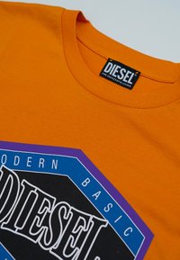 Oranje Diesel t-shirt met een ronde hals en een gedurfde grafische logo in zwart, blauw en paars met de tekst "Modern Basic Diesel."