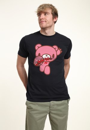 Ung mand med uplejet blondt hår iført en sort t-shirt med en pink bjørn med røde mærker i ansigtet og på poten.