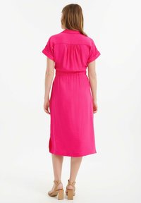 Abito rosa a maniche corte con vita accentuata da una cintura, orlo al ginocchio e spacchi laterali, realizzato in tessuto testurizzato. Sandali con tacco e dettaglio alla cinghia.