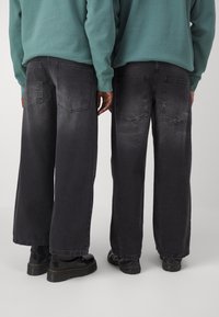 Czarne dżinsy o szerokich nogawkach z wyblakłą teksturą, dwoma tylnymi kieszeniami i kontrastowymi szwami. Połączone z czarnymi butami i turkusową bluzą.