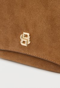 Καφέ σουέντ τσάντα χειρός με χρυσαφί λογότυπο και ραμμένα άκρα. Ομαλή υφή με μινιμαλιστικό σχεδιασμό.