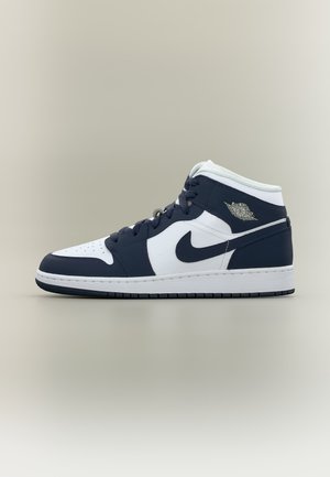 Średni sneaker Nike Air Jordan w białym i ciemnoniebieskim kolorze, z czarnymi sznurowadłami, gumową podeszwą oraz logo skrzydeł Air Jordan na kostce.
