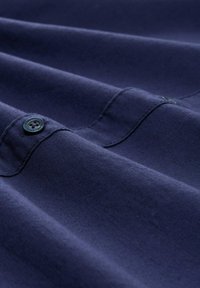 Tejido de color azul marino con una textura suave, que presenta un detalle de botón. El material parece liso con costuras y pliegues sutiles.